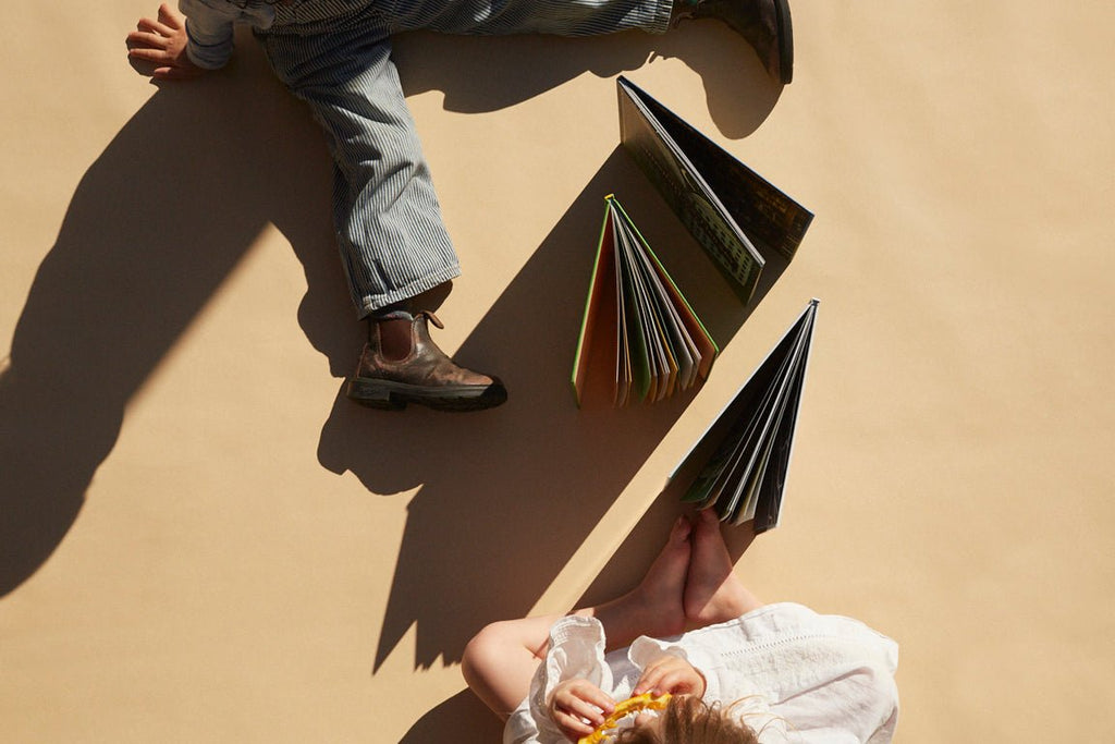 Two people sitting on a beige surface with books open in front of them, casting shadows.