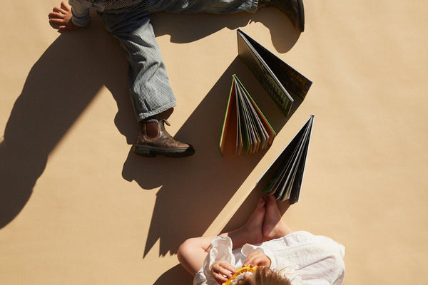 Two people sitting on a beige surface with books open in front of them, casting shadows.