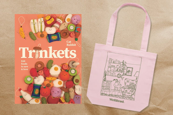 Book titled 'Trinkets' with colorful illustrations and a pink tote bag with a black and white design on a beige background.