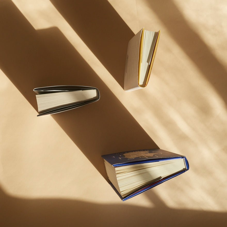 Three books of different sizes on a beige surface with shadows